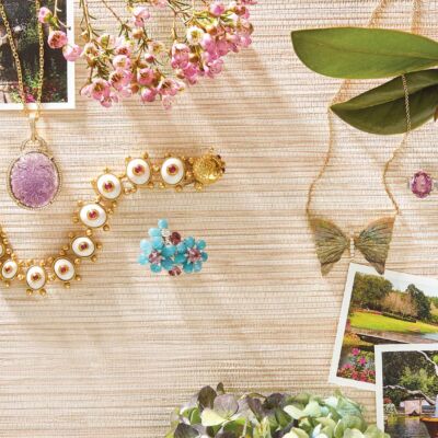 A green bejeweled butterfly, a purple pendant, and a ruby bracelet lay next to pictures of a green garden.
