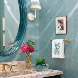 Two small flower arrangements atop pink-veined marble countertop in Nellie Howard Ossi designed powder room.