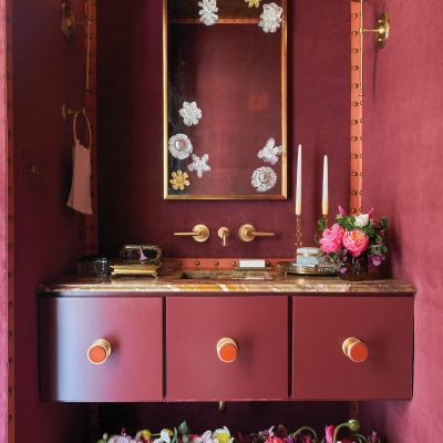 A maroon colored bathroom with flowers at the sink.