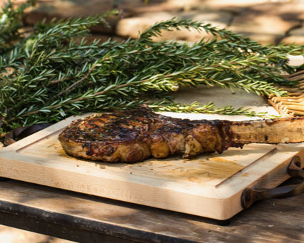 Grilled Steak la Zaca on wooden cutting board with bunch of rosemary