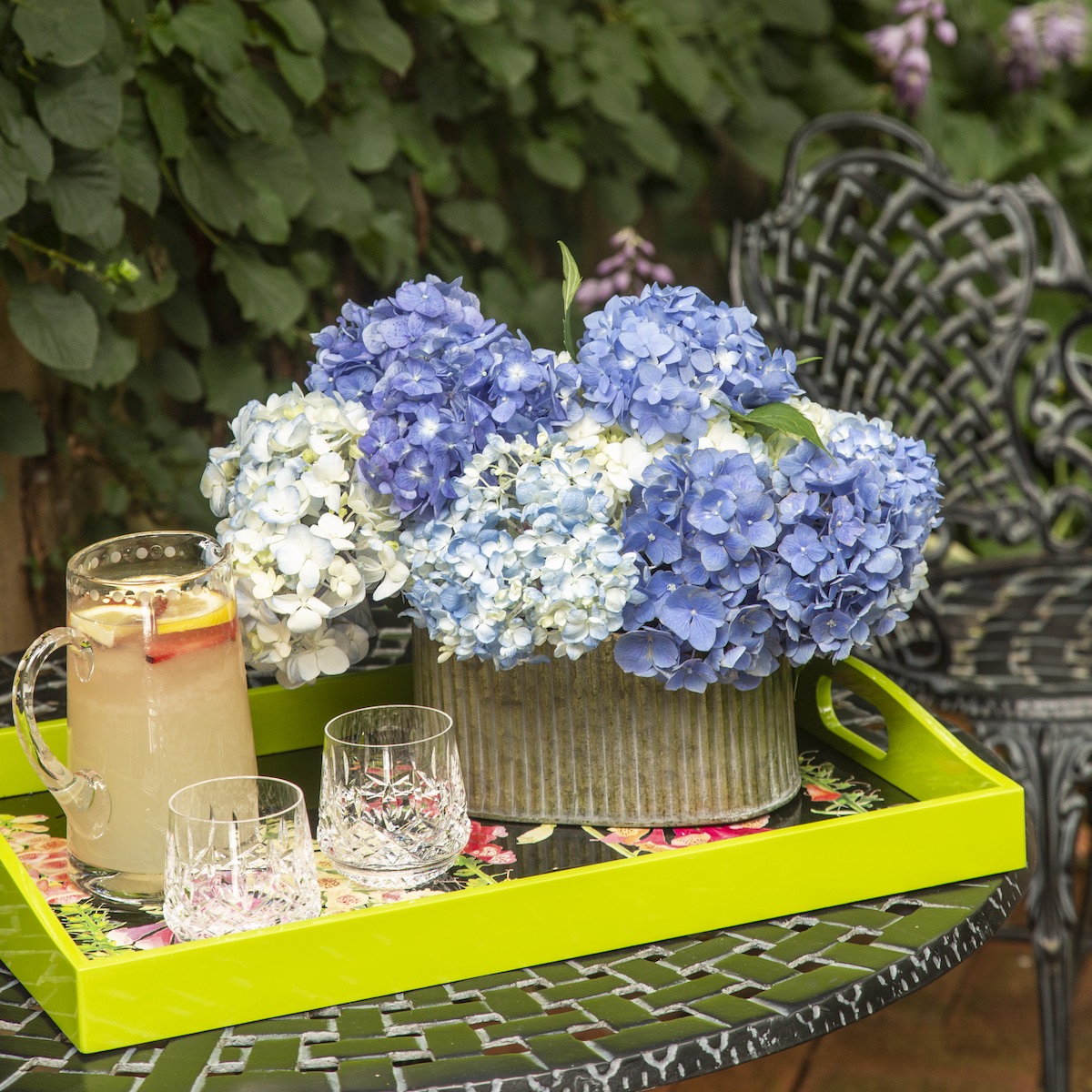 Arrangement of blue and white hydrangeas in a galvanized container next to a pitcher of white sangria on a chartreuse tray.