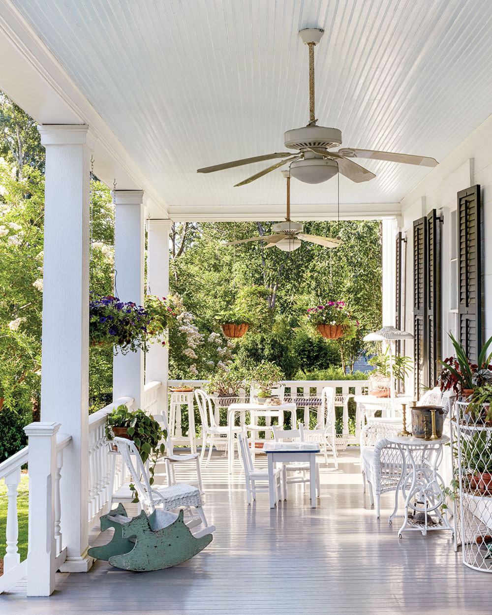 Back porch with white columns, ceiling fans, white furniture, and hanging baskets of flowers