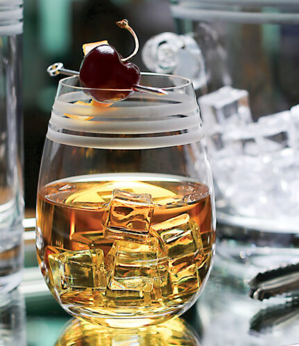 bourbon on the rocks in a crystal wine tumbler, garnished with a cherry on a pick