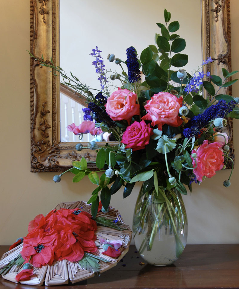 vase of flowers, displayed in front of a gilt framed mirror, beside a vintage flower-bedecked hat