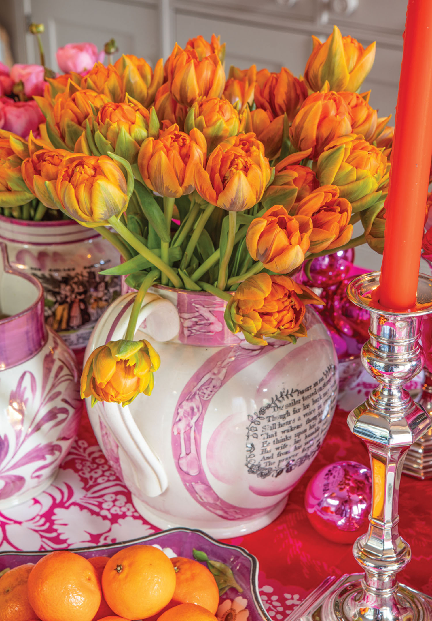 Orange tulips, candlesticks, and citrus dazzle against the pink tablecloth.