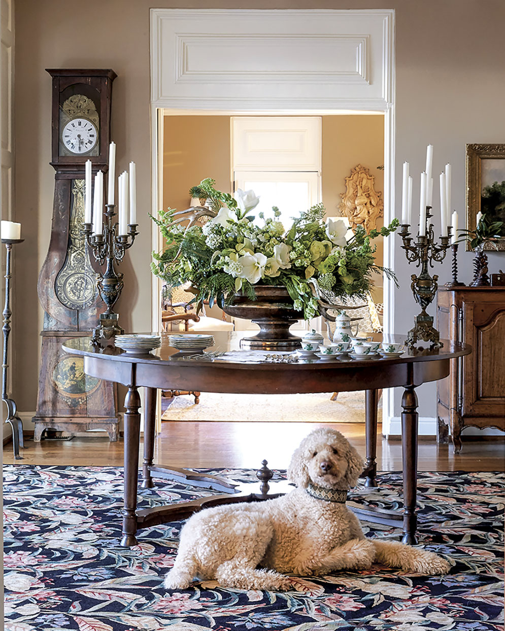 Grand green and white holiday floral design by  Kakhi Huffaker Wakefield of K Wakefield Designs, placed on a round entry table in an elegantly styled foyer. A dog lies beneath the table