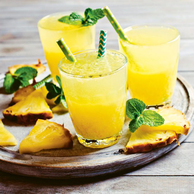 pineapple mocktails on wooden tray with slices of pineapple and mint garnish