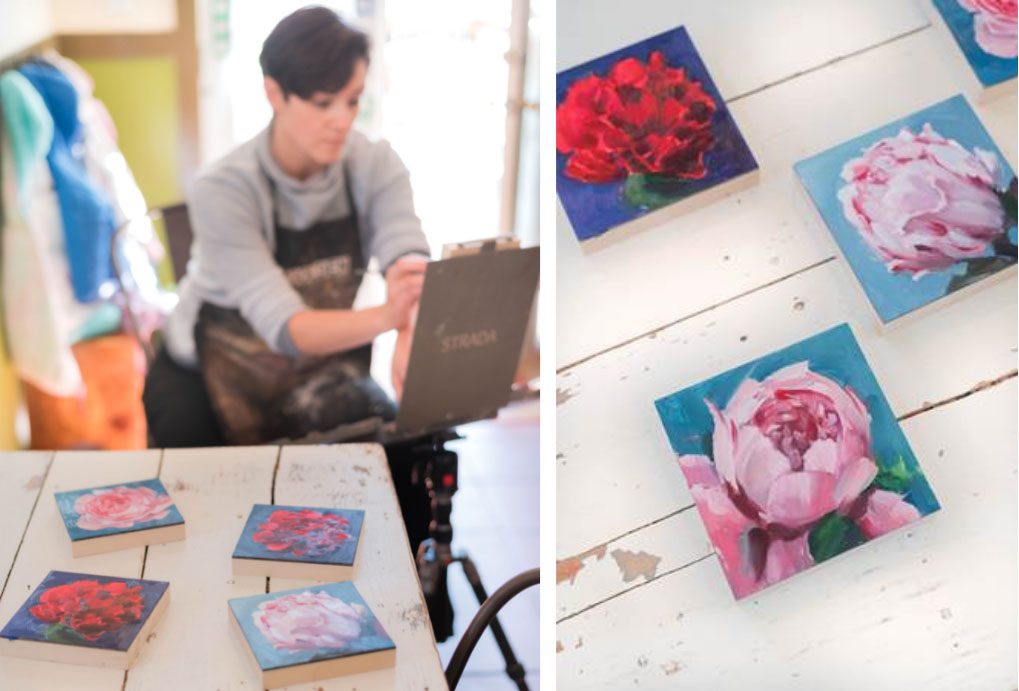 Artist Amy R. Peterson paints at an easel in the background. In the four ground, four paintings of peonies from her Peony Project are displayed on a rustic white table.