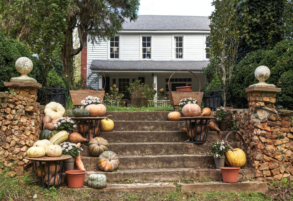 A display of pumpkins and other squash in cream, pale orange, and yellow decorate steps flanked by stone pillars. In the background is Keith Robinson's two-story white farmhouse
