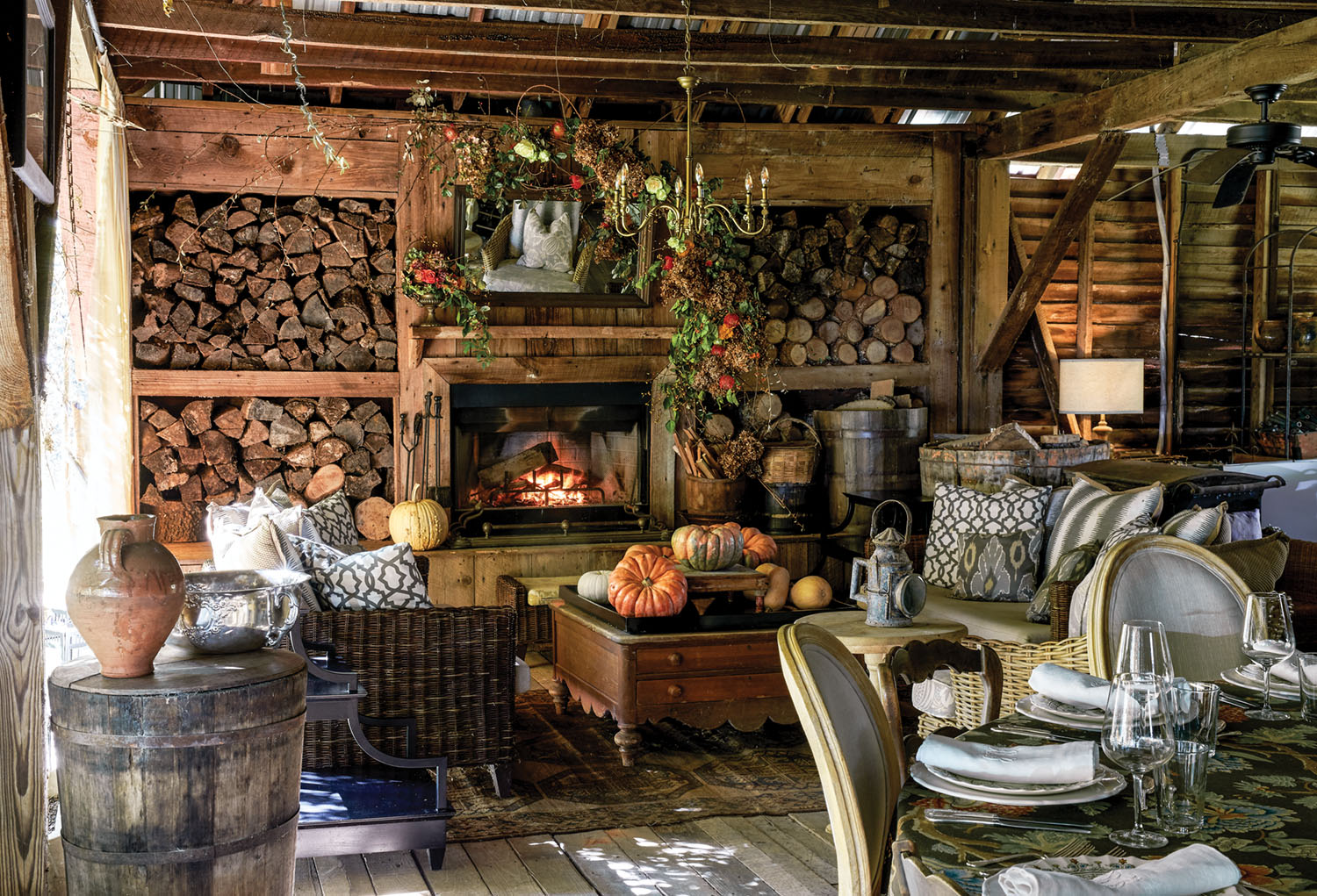 At Keith Robinson's home at Redwine Plantation, a large room with barnwood walls, floors, and ceilings. Ample firewood is stored in cubbies surrounding the hearth. Autumn floral arrangements, garlands, and pumpkins decorate the hearth and comfortable seating area.