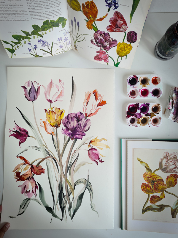 watercolor of spring bulb flowers by Safiyyah Choycha. Botanical reference books and watercolor paints show the artist's tools of the trade