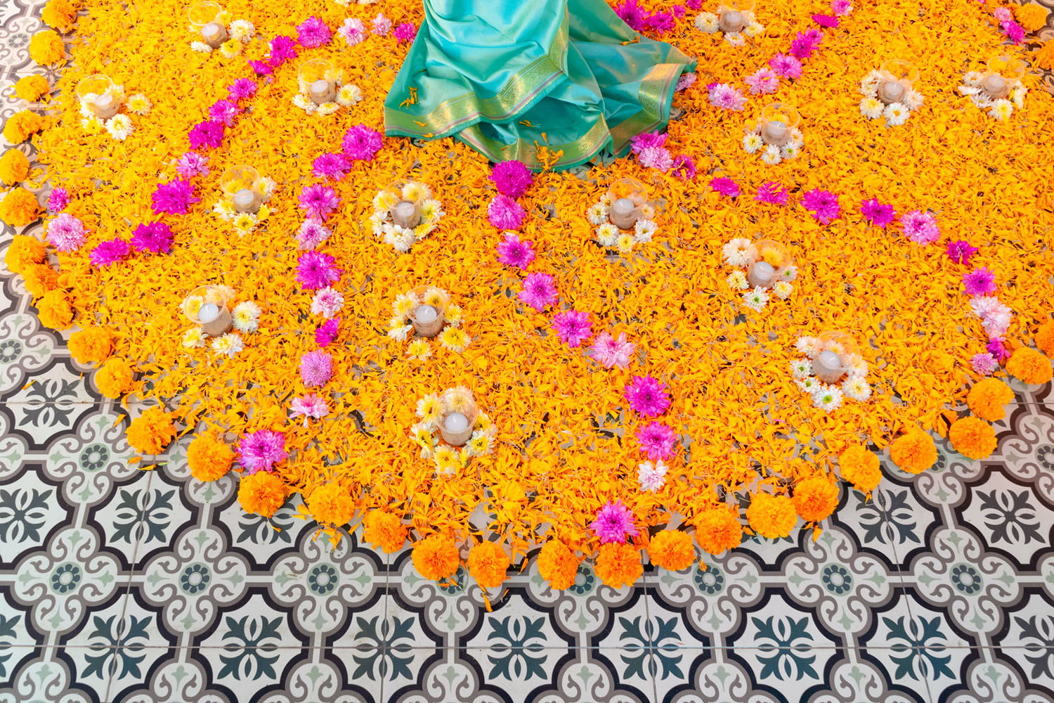 a vibrant circular, symmetrical design of orange marigold blooms and petals, accented with pink flowers, on an ornate tile floor