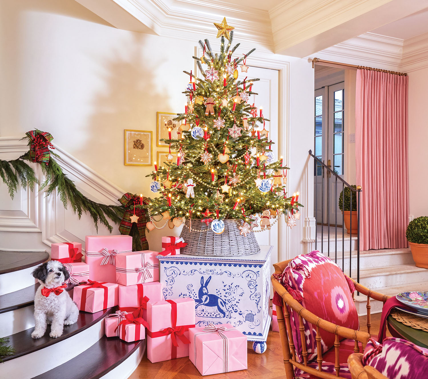 Christmas presents wrapped in pink paper and tied with red or silver ribbon are stacked on the stairs beside a tabletop tree set on a blue-and-white toy chest.