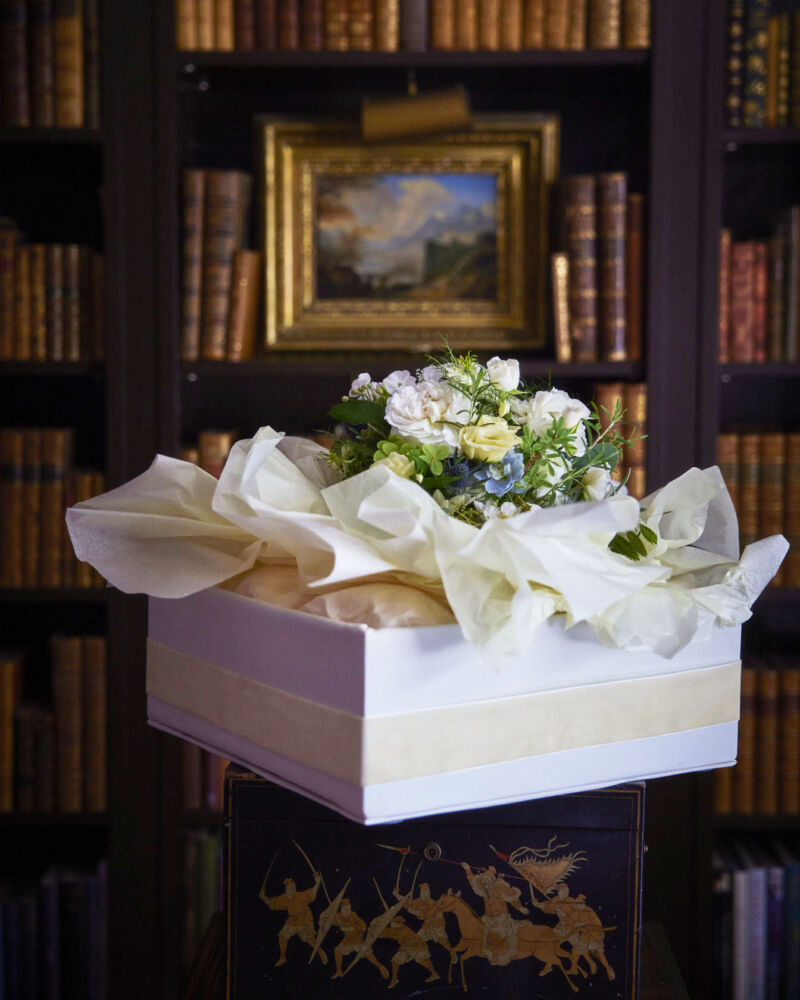 India Hicks's Wedding Party Flowers, bouquet set in tissue paper in a white box, with a moody English home library in the background