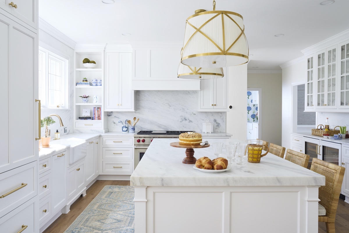 Brass-trimmed drum pendant lights over large white marble topped island in kitchen.