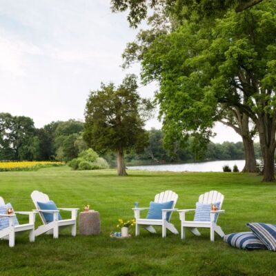White Adirondack chairs sit on a grassy shore front.