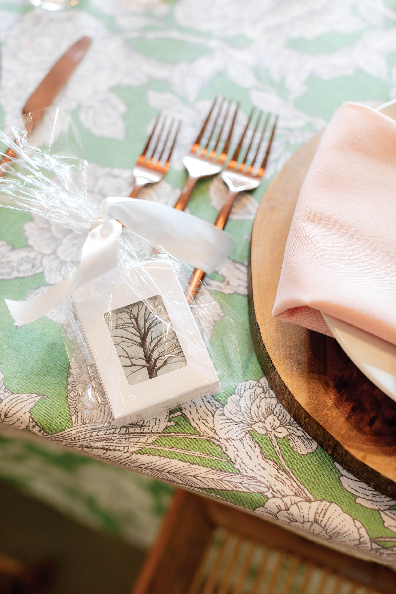 Silverware is tied with a ribbon and a deck of playing cards while sitting on top of a green floral table cloth.