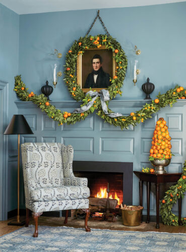 A blue room and fireplace mantel are decorated with greenery and oranges.