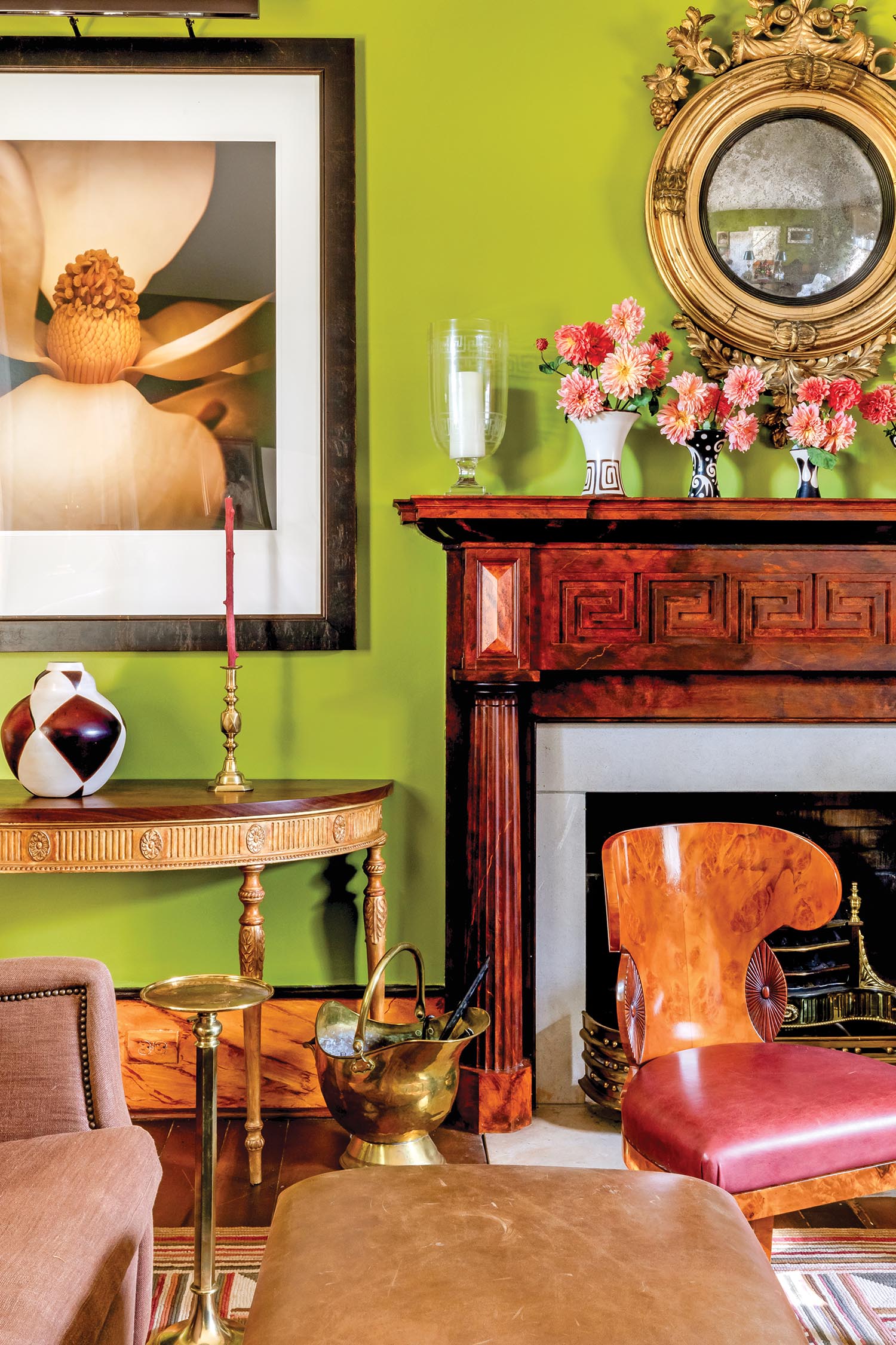 A bright green parlor is filled with golden brown antiques, a floral photograph, a gold mirror, and pink dahlias on the mantel.