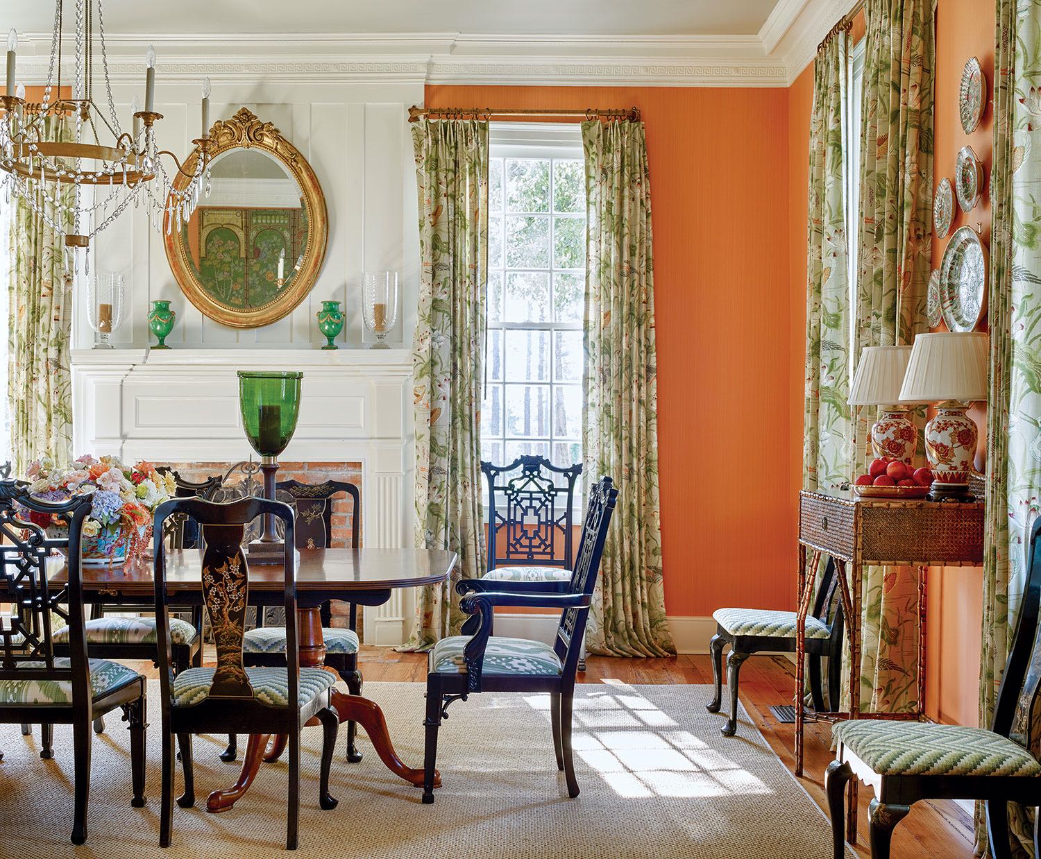 Dining room designed by James Farmer at McCurdy Plantation, featuring apricot walls, botanical-patterned curtains, a white-painted fireplace mantel and crown molding and a neutral area rug.