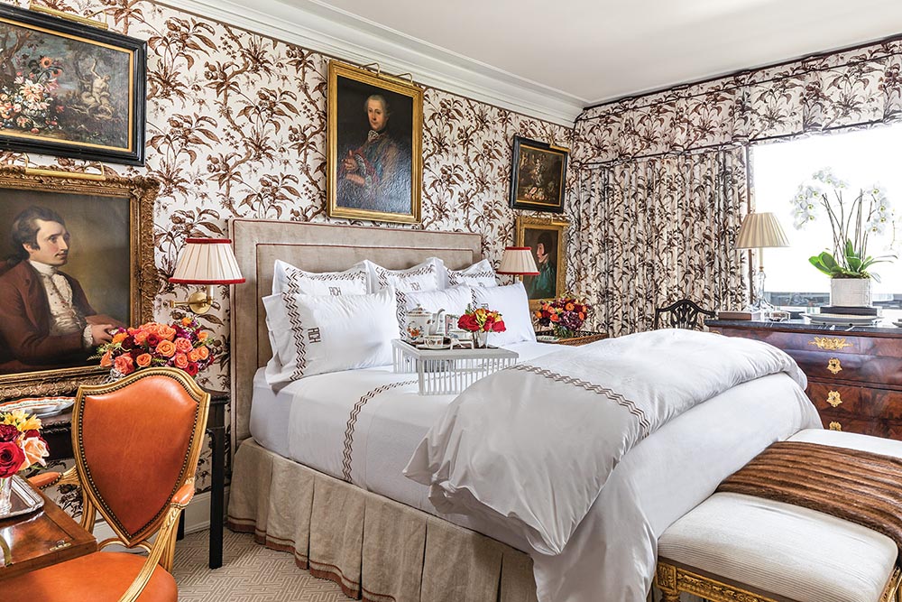 The bedroom has brown floral wallpaper with portraits hanging.