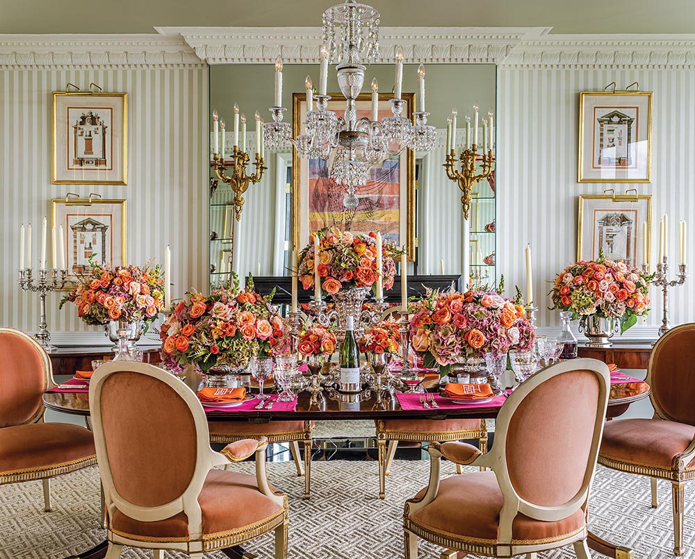 Velvet amber chairs are around an oval table in a dining room with many orange rose arrangements.