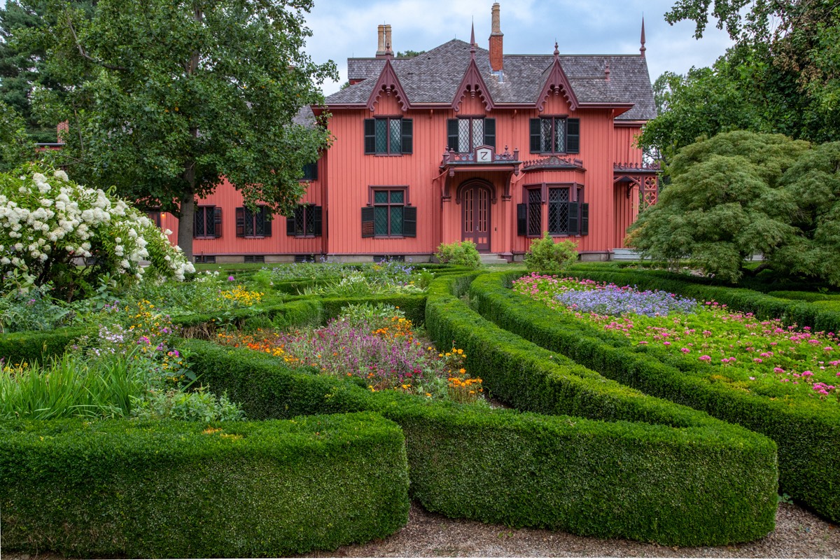 A bright red Victorian house sits behind a winding garden of green hedges at historic Roseland Cottage from Connecticut Gardens.