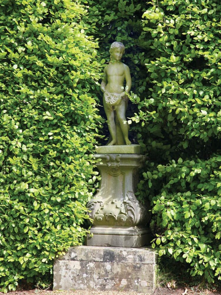 Statue of a child standing tucked into the hedge at Ditchley house