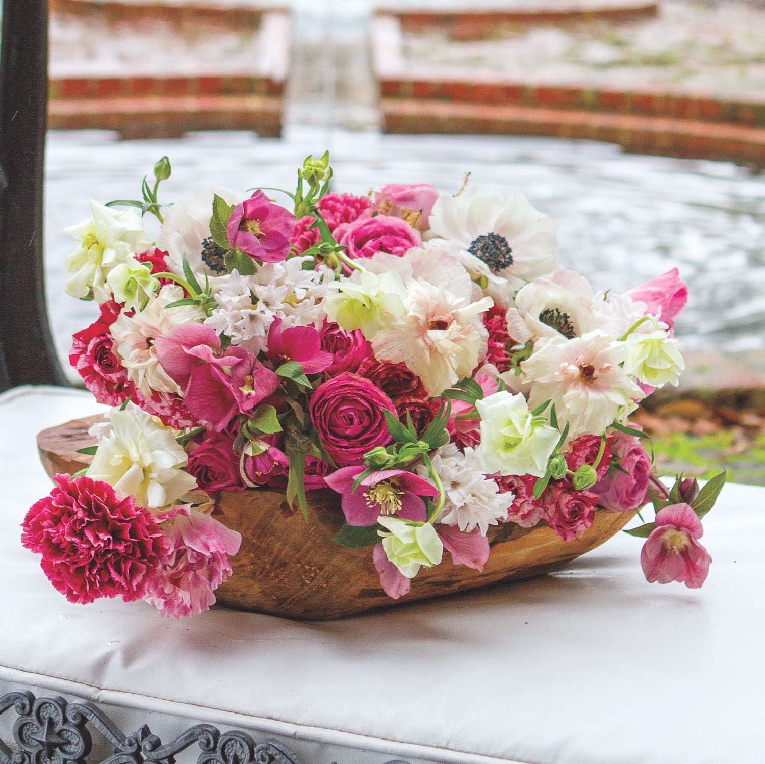 Kim Starr Wise fills a wooden bowl with pink flowers: Japanese ranunculus, anemones, hyacinths, carnations, hellebores, and garden spray roses in hues of pink.