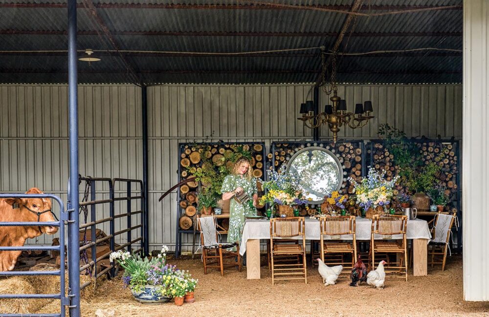 Denise McGaha sets a table inside a barn with chickens and a cow.