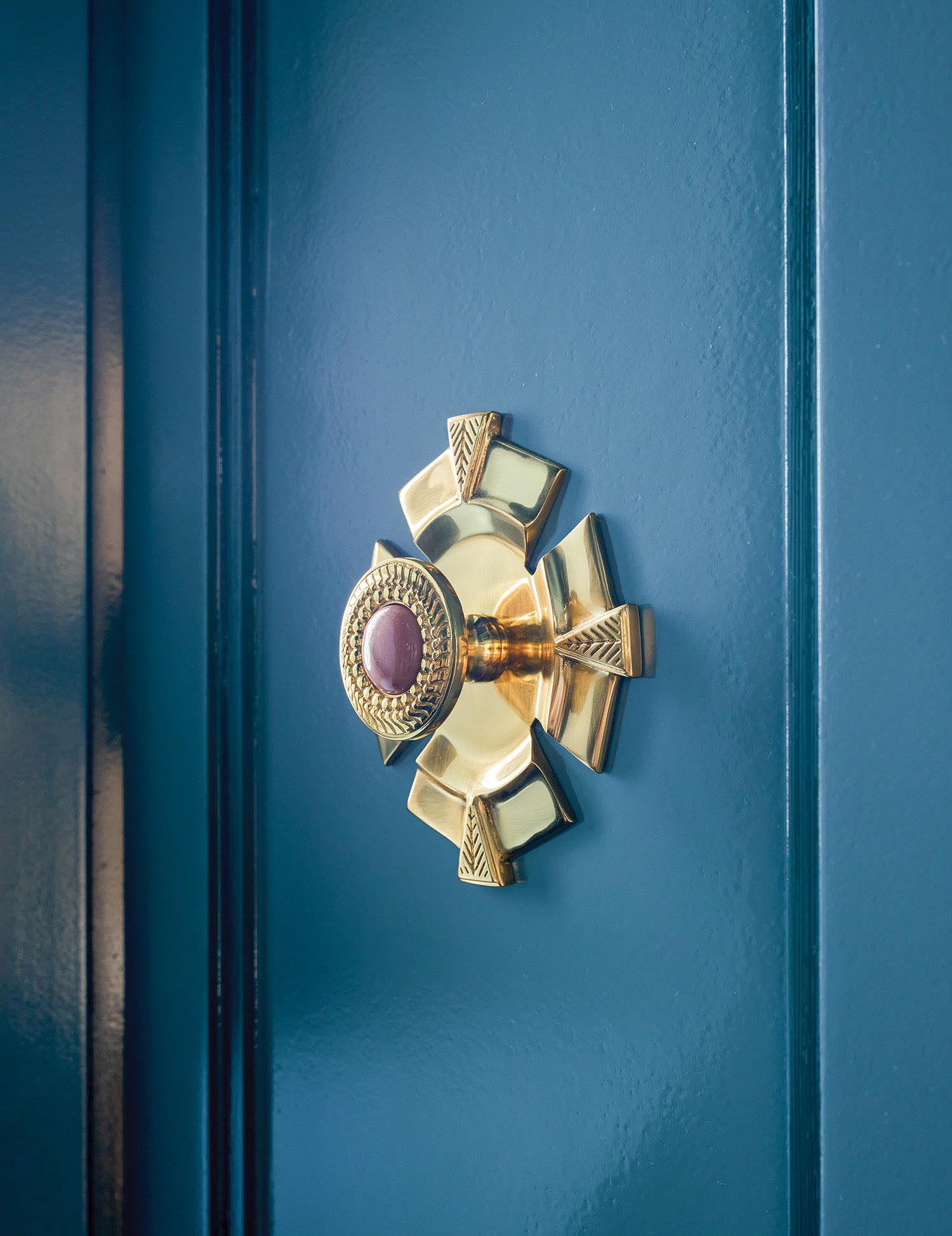 A gold knob with a purple jeweled center on a blue cabinet.