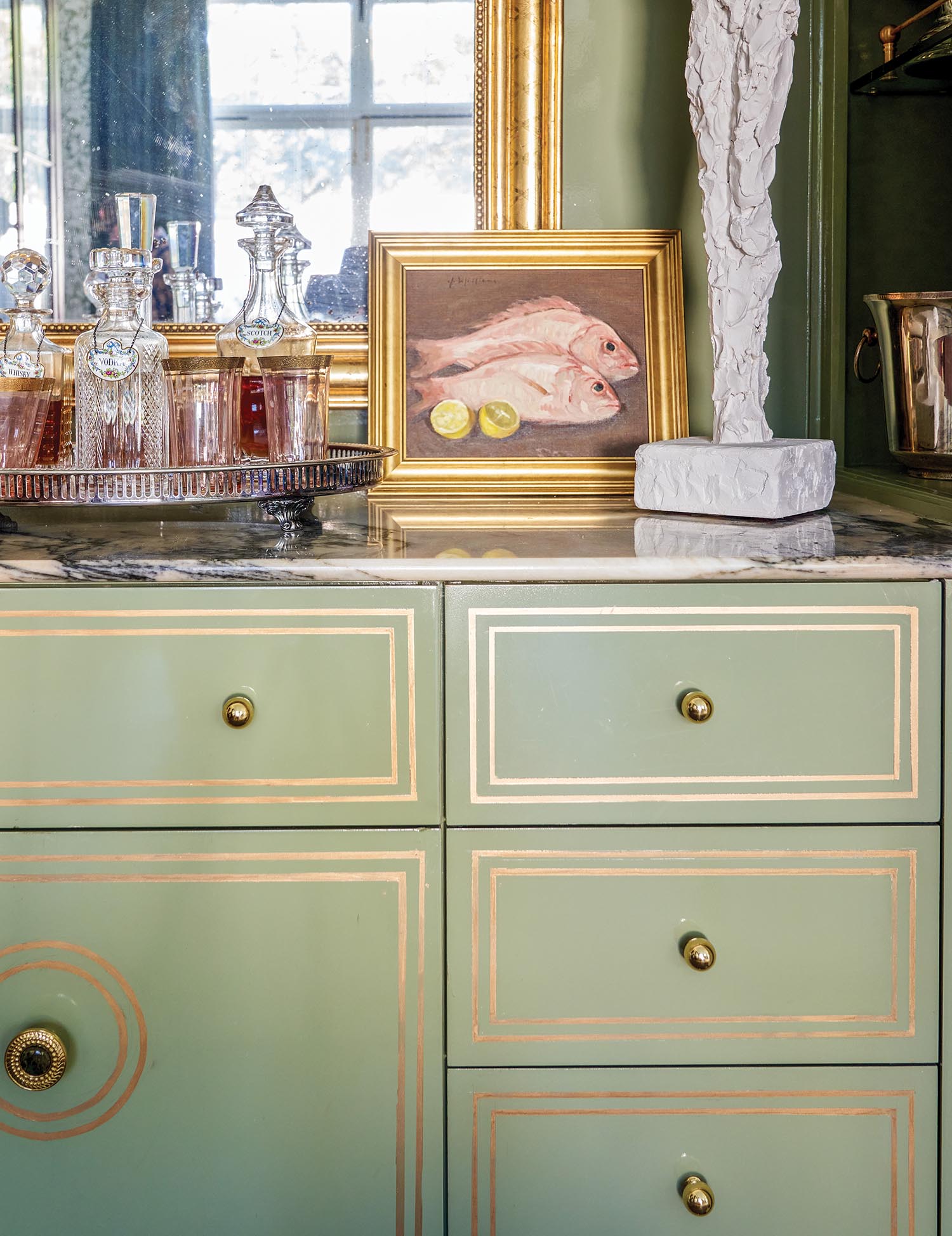 A green cabinet has gold painted accents and knobs.