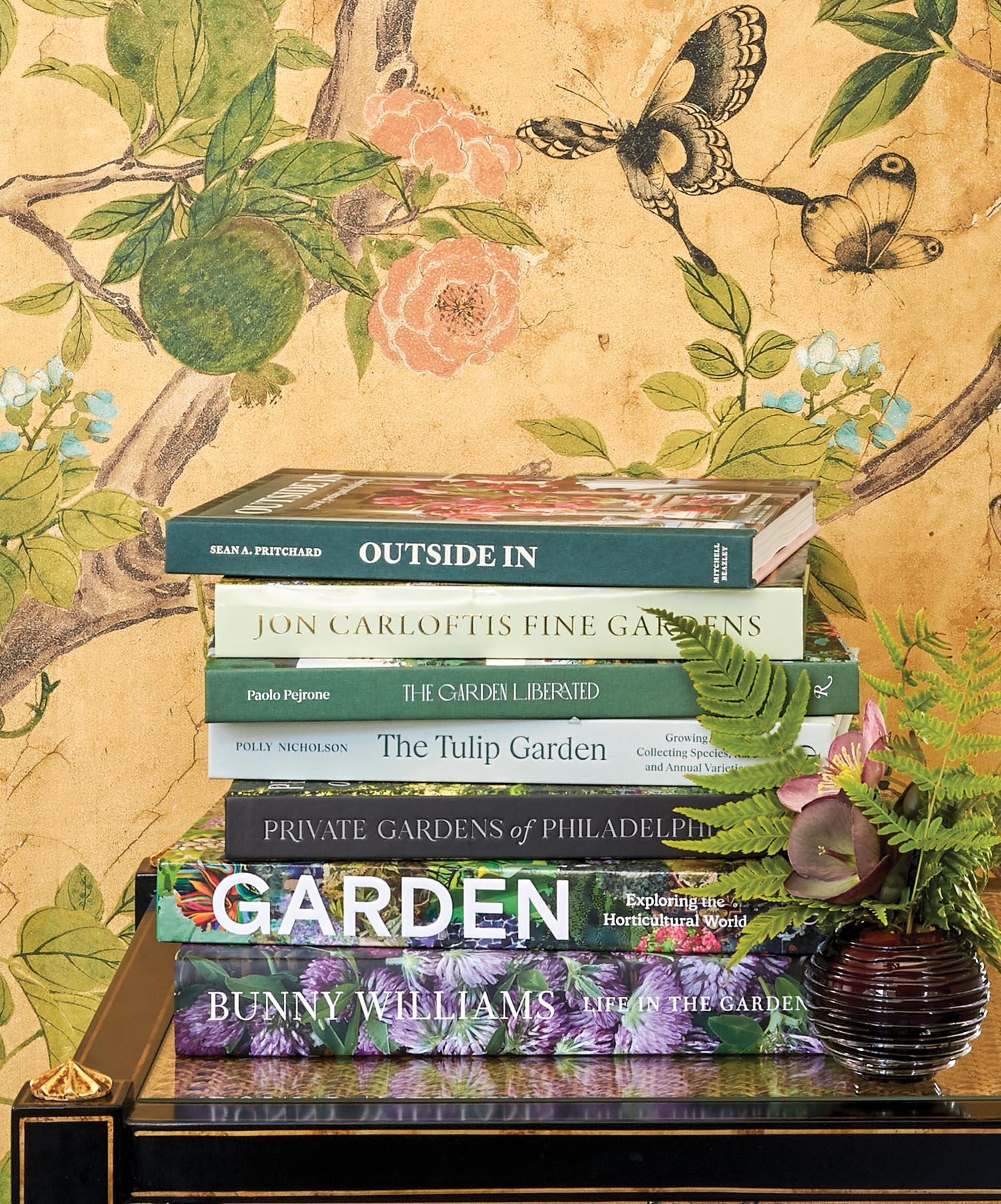A pile of books in front of floral wallpaper.