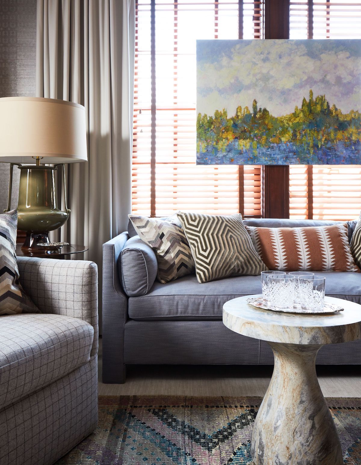A contemporary blue sofa cozies up to a traditional plaid swivel chair while a marble coffee table exudes both modern and classic sophistication. Colorful accents come in through the art, rug, and geometric pillows.