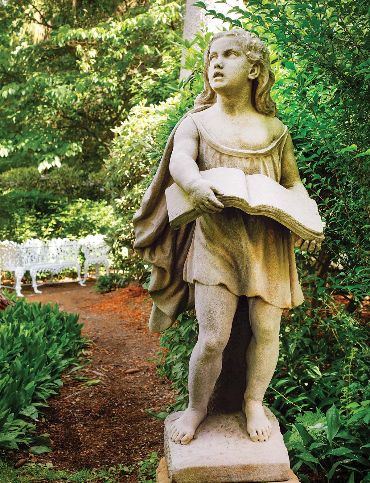 A statue of a child holding a book stands in the garden.