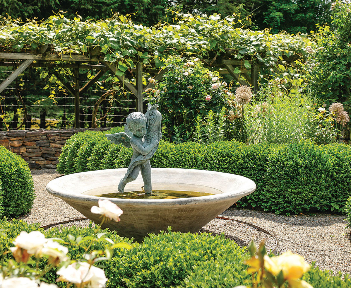 A cherub statue is in a fountain in a garden.