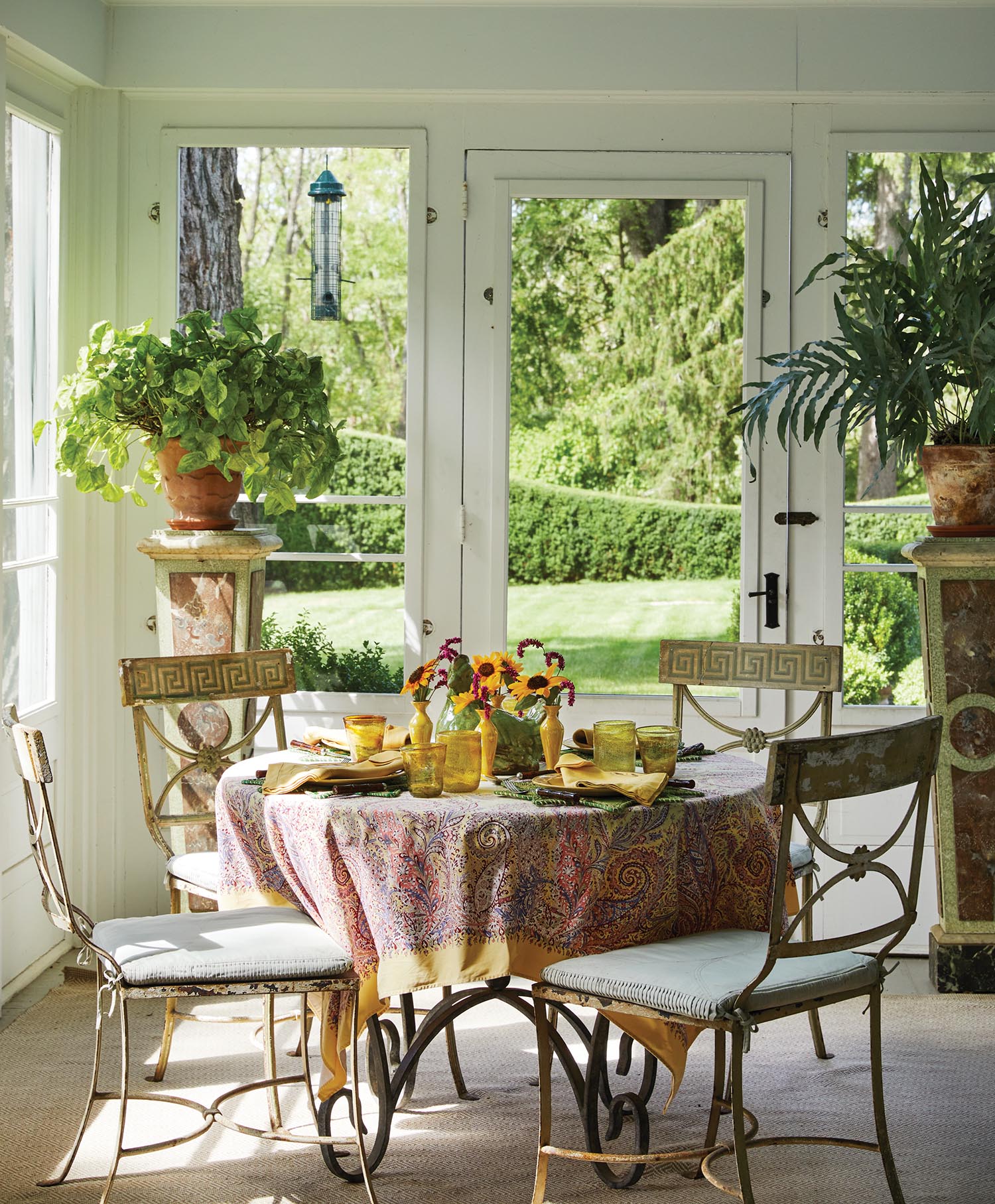 A table is set in a sunroom with a pink tablecloth and sunflowers.