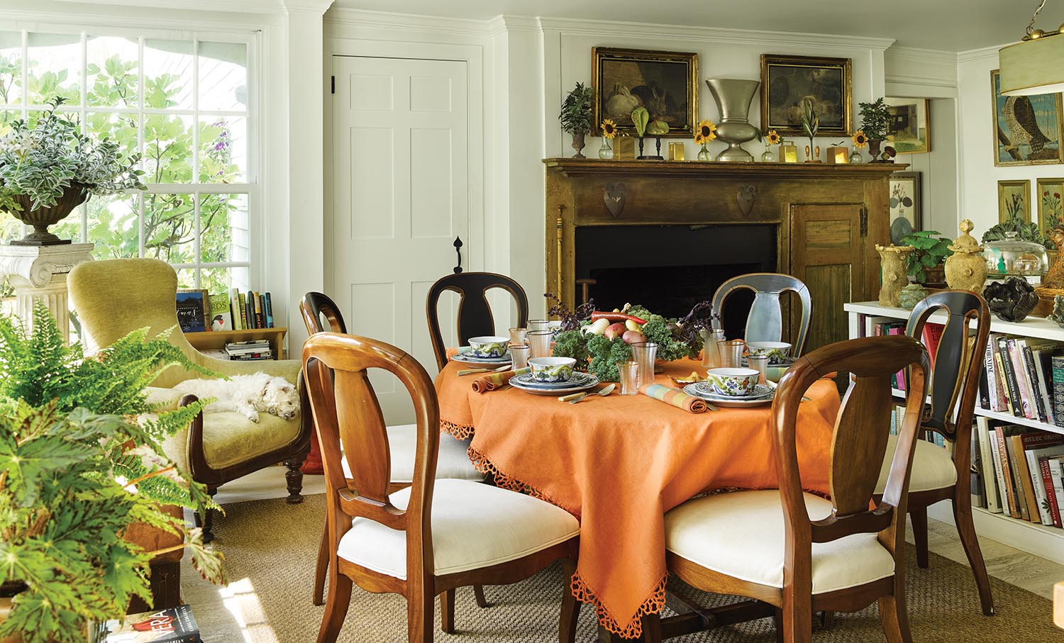 A round table is set up near a fireplace with an orange tablecloth and is set for tea.