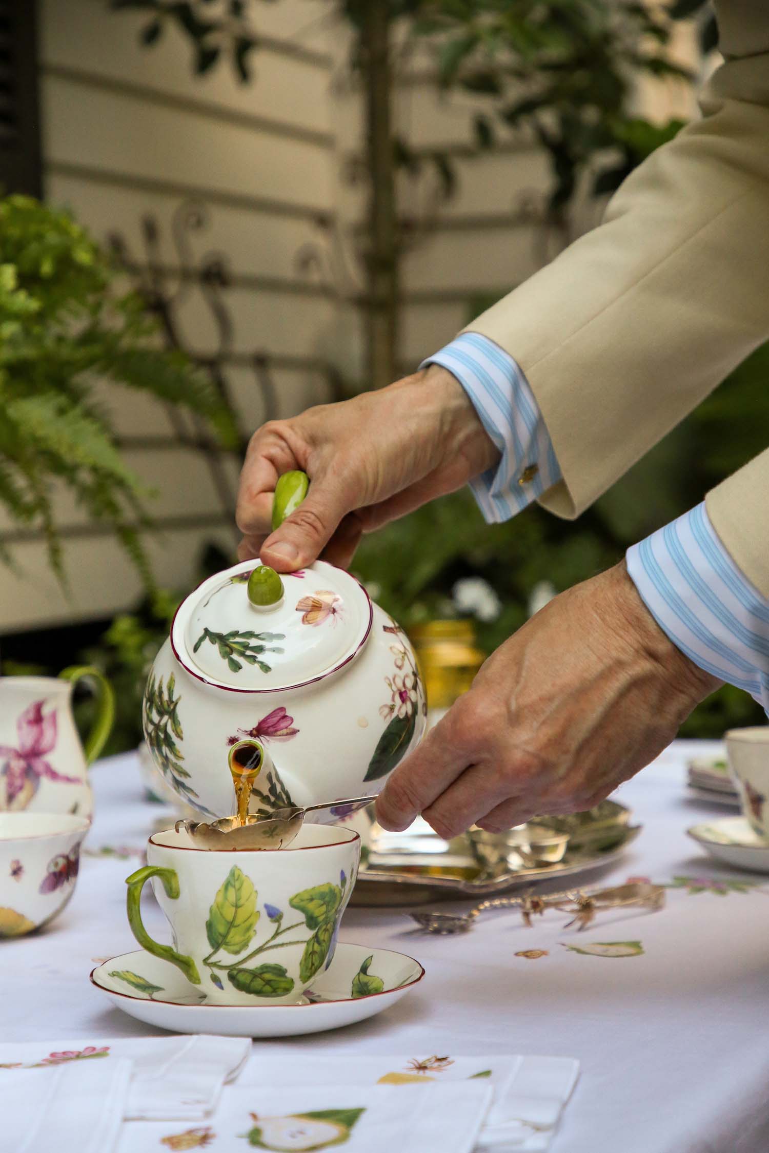 Hands pouring a floral ceramic teapot.