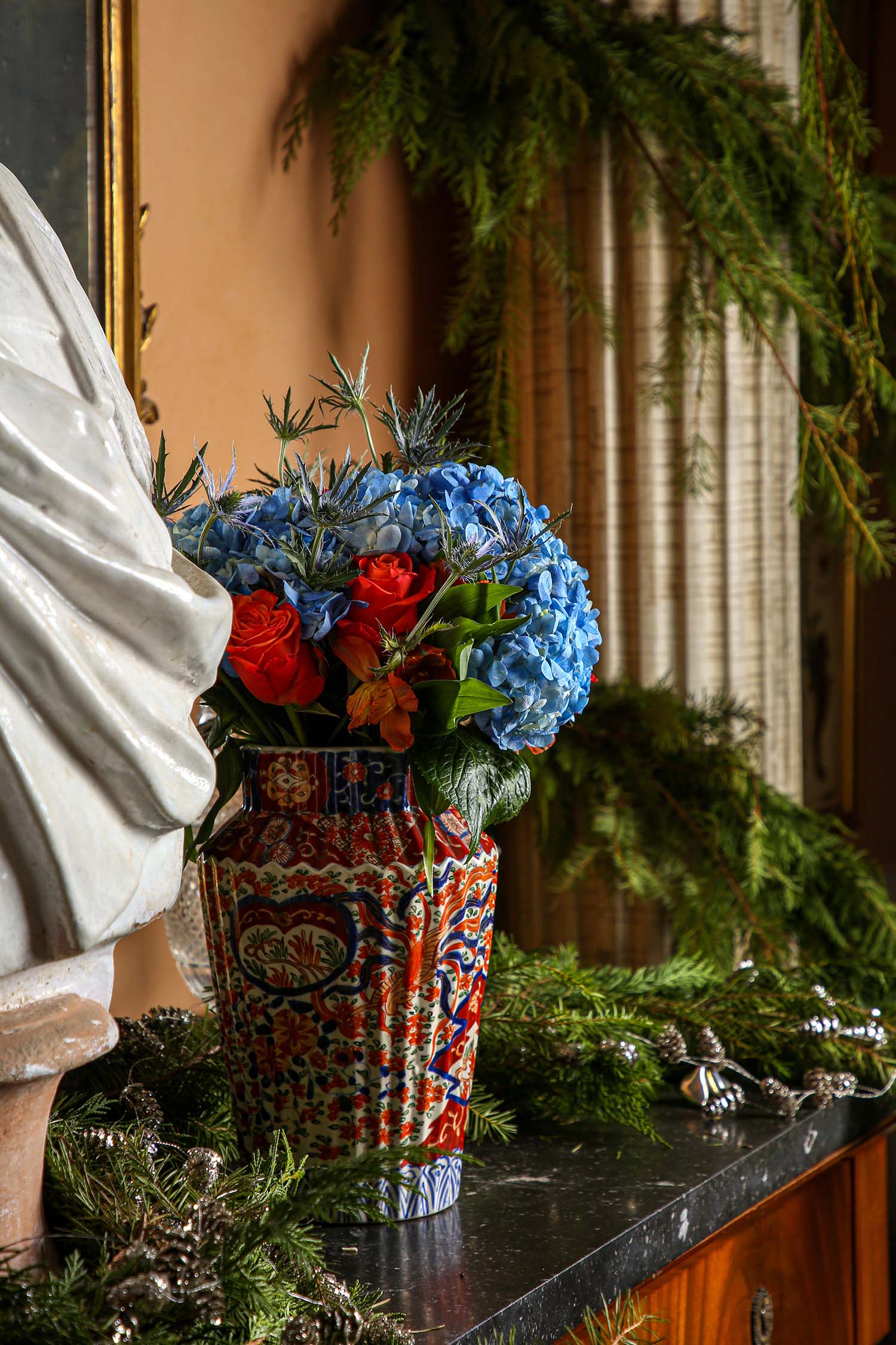 Blue hydrangeas contrast with red roses in an Imari vase.