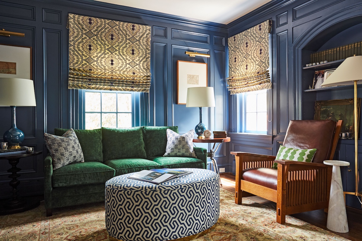 Moody, navy den for a business executive that features a plush velvet green sofa; handsome leather Stickley chair and a curated library collection