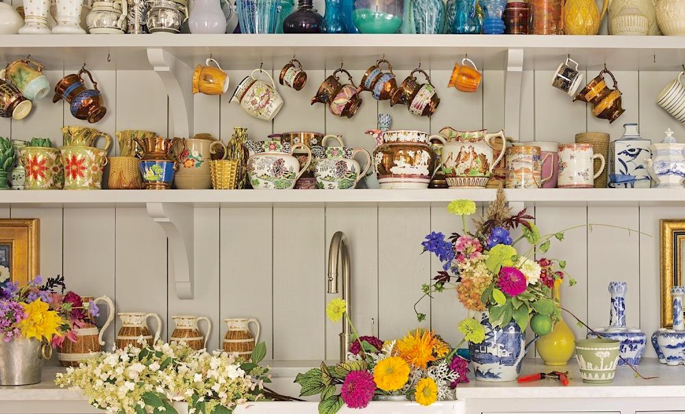 Shelves filled with mugs, vases, and teapots for flower arrangements over a sink filled with flowers in Bunny Williams' flower room. 