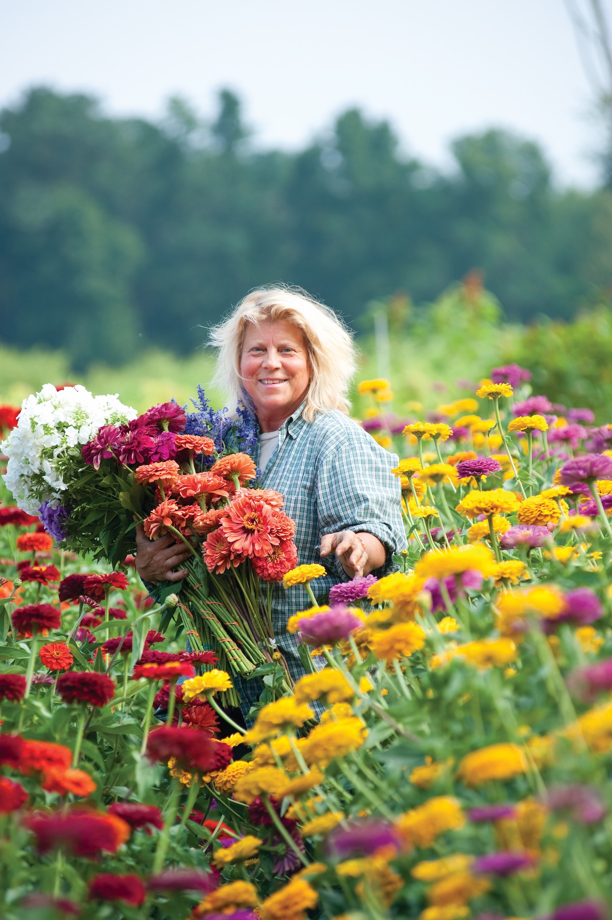 Marilyn Cederoth standing in field of zinnias, holding armful of flowers